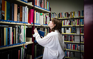Studentin nimmt ein Buch aus dem Regel